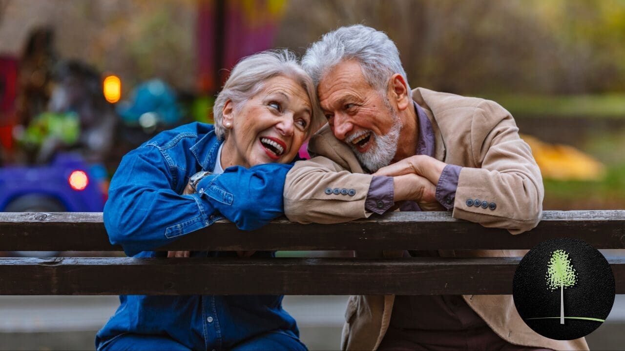 An elderly couple sitting on a park bench, smiling and enjoying a sunny day, symbolizing financial stability and peace of mind in retirement.